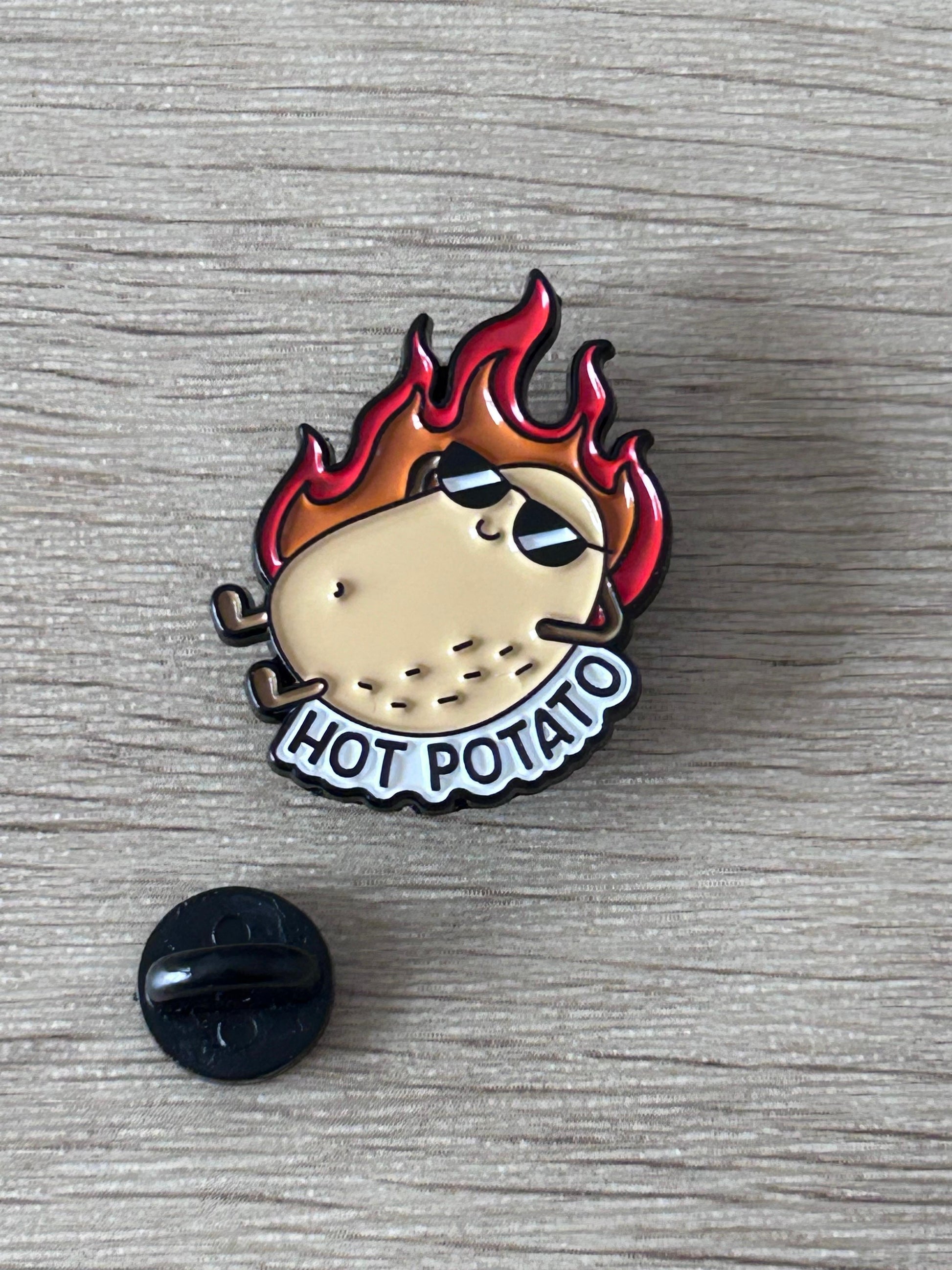 Épingle émaillée patate en flammes avec inscription HOT POTATO et attache noire.