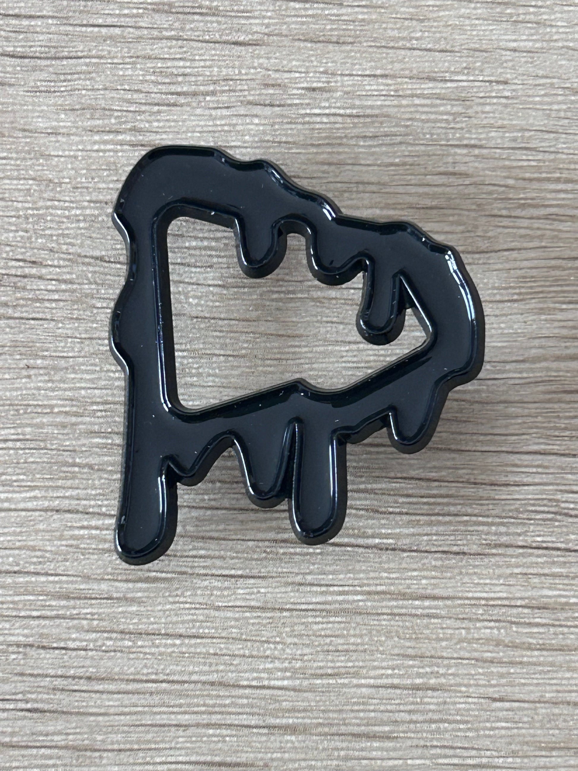 Épinglette noire en forme de silhouette dégoulinante