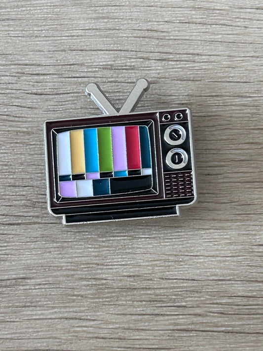 Broche en forme de télé vintage, à mire colorée sur fond noir.