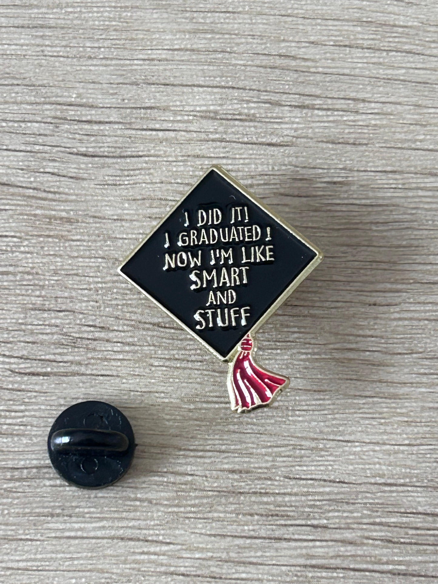 Épinglette toque de diplômé: losange bleu nuit, texte blanc, pompon rouge, fixation noire.