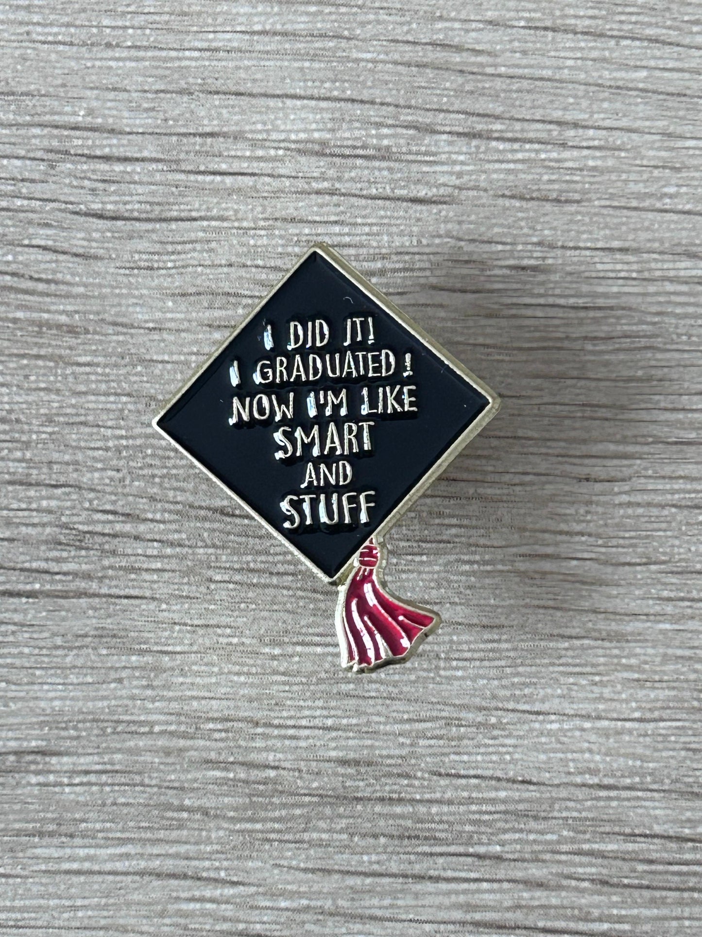 Épinglette toque de diplômé: losange bleu nuit, texte blanc «SMART AND STUFF», pompon rouge.