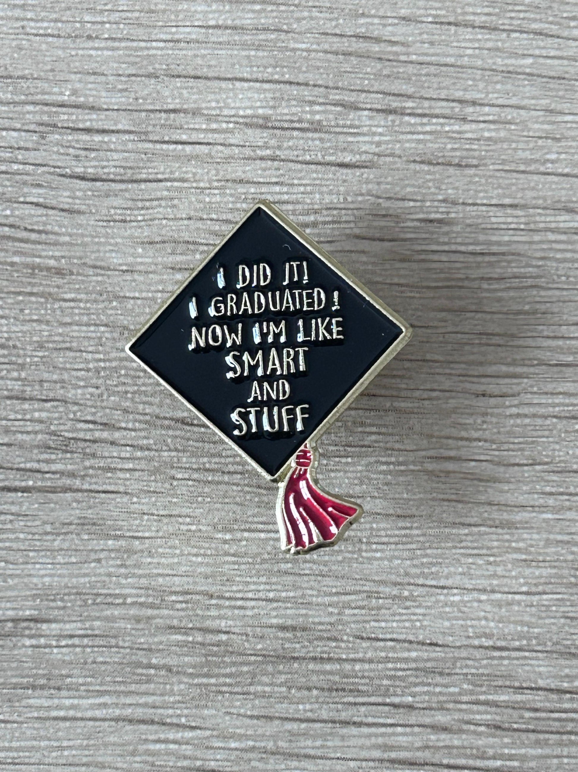 Épinglette toque de diplômé: losange bleu nuit, texte blanc «SMART AND STUFF», pompon rouge.