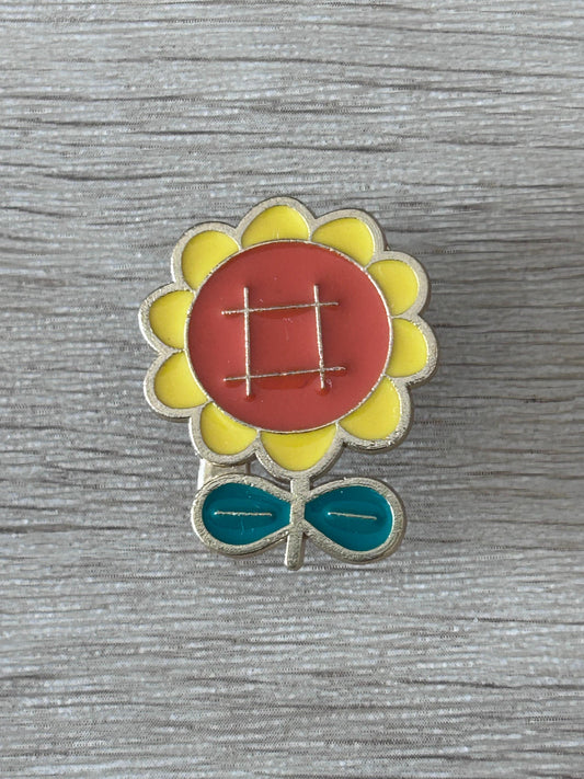 Broche tournesol en émail : centre rouge quadrillé, pétales jaunes, feuilles vertes.