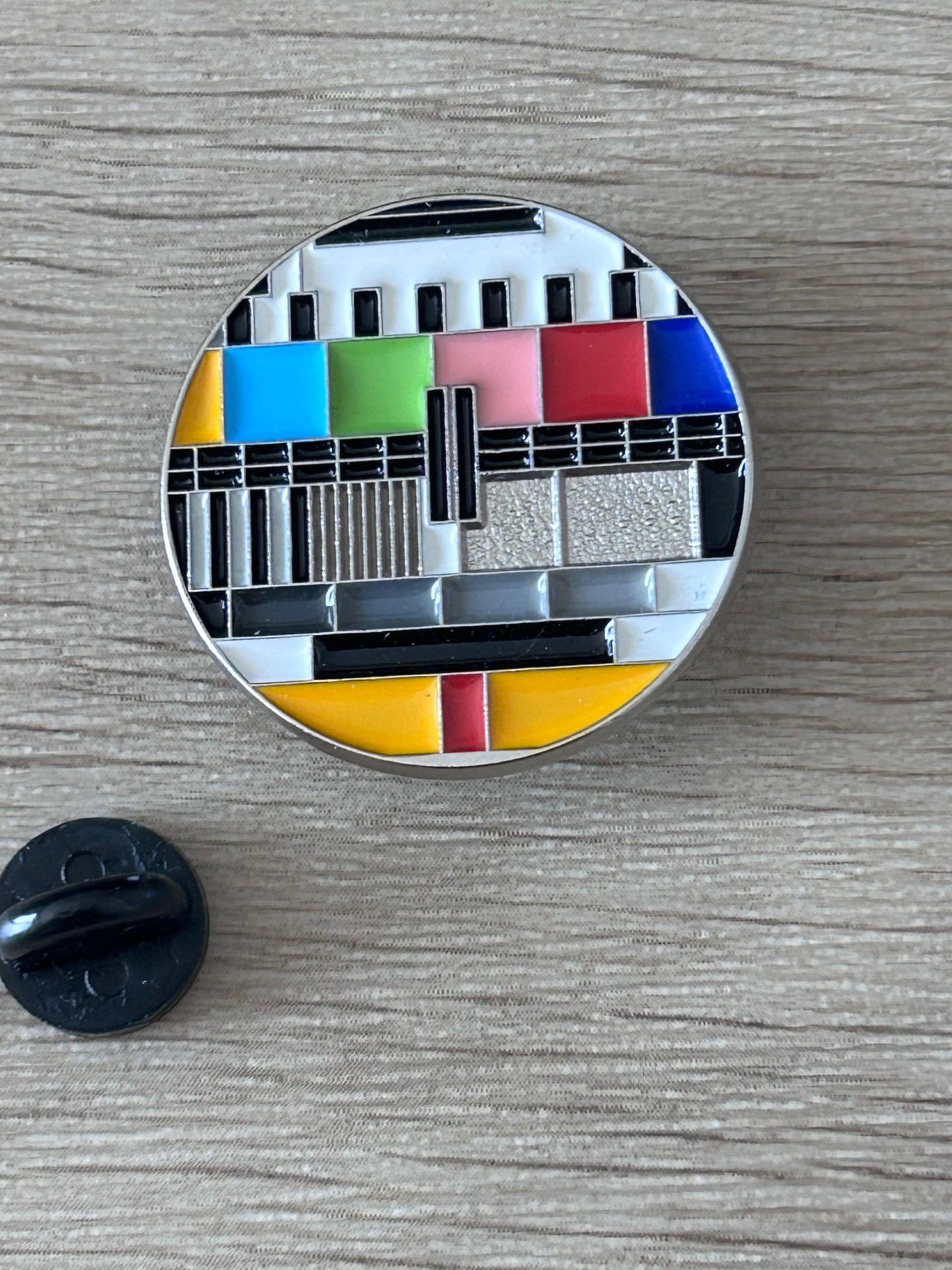 Pin's rond mire TV colorée, avec partie arrière noire visible