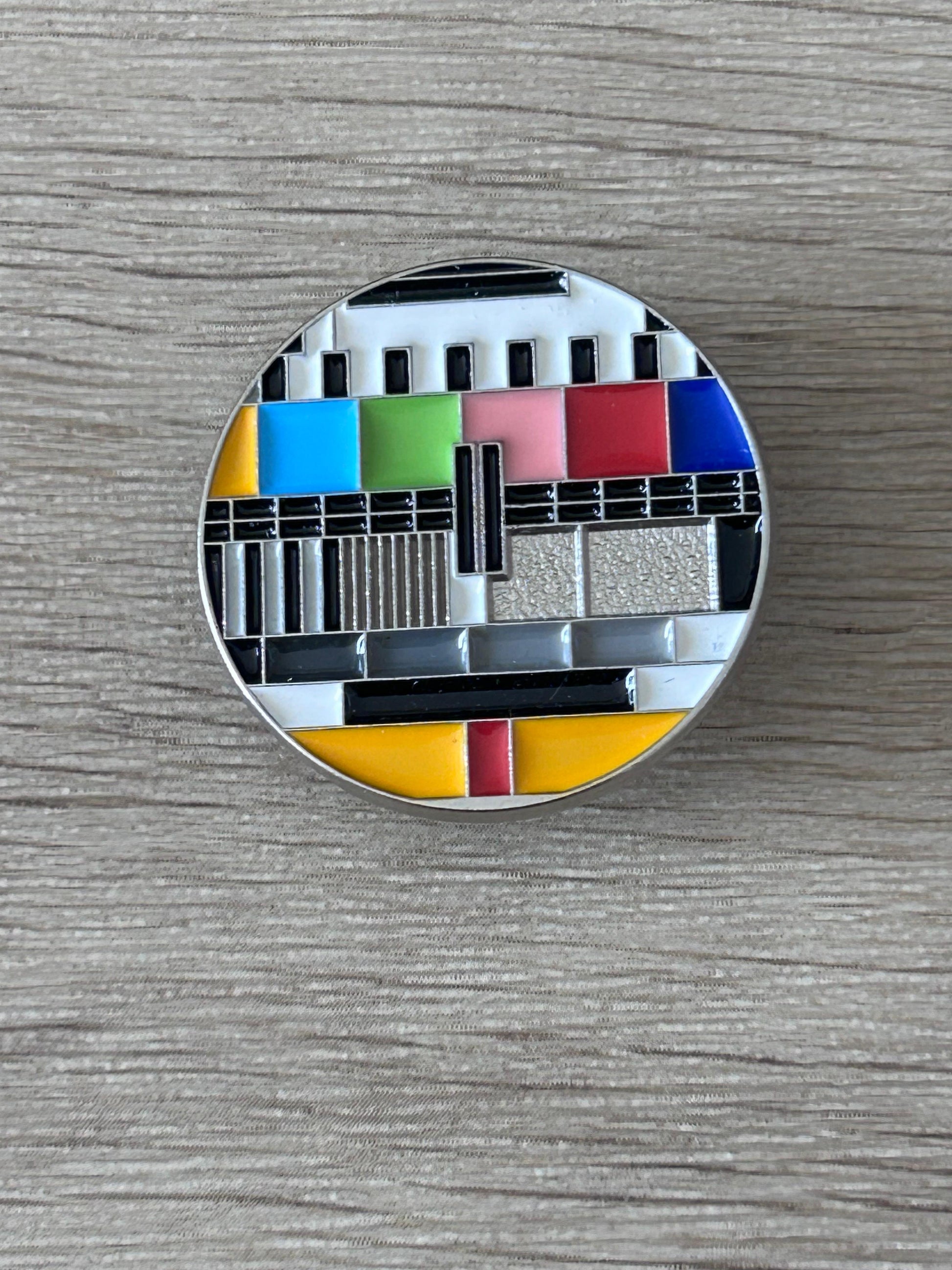 Pin's rond avec motif mire TV en bandes colorées et fond argenté
